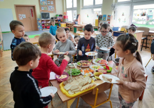 Siedmioro dzieci nakłada na talerzyki wybrane przez siebie potrawy ze stołu szwedzkiego